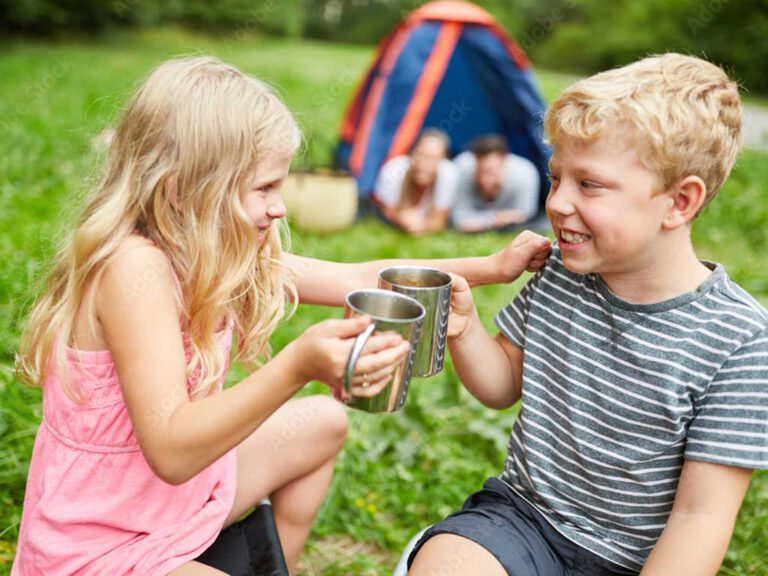Das Bild zeigt zwei Kinder im Grundschulalter beim Camping in der Natur mit ihren Eltern im Zelt im Hintergrund, als Vorschau für den Eltern-Workshop Endlich Ferien.