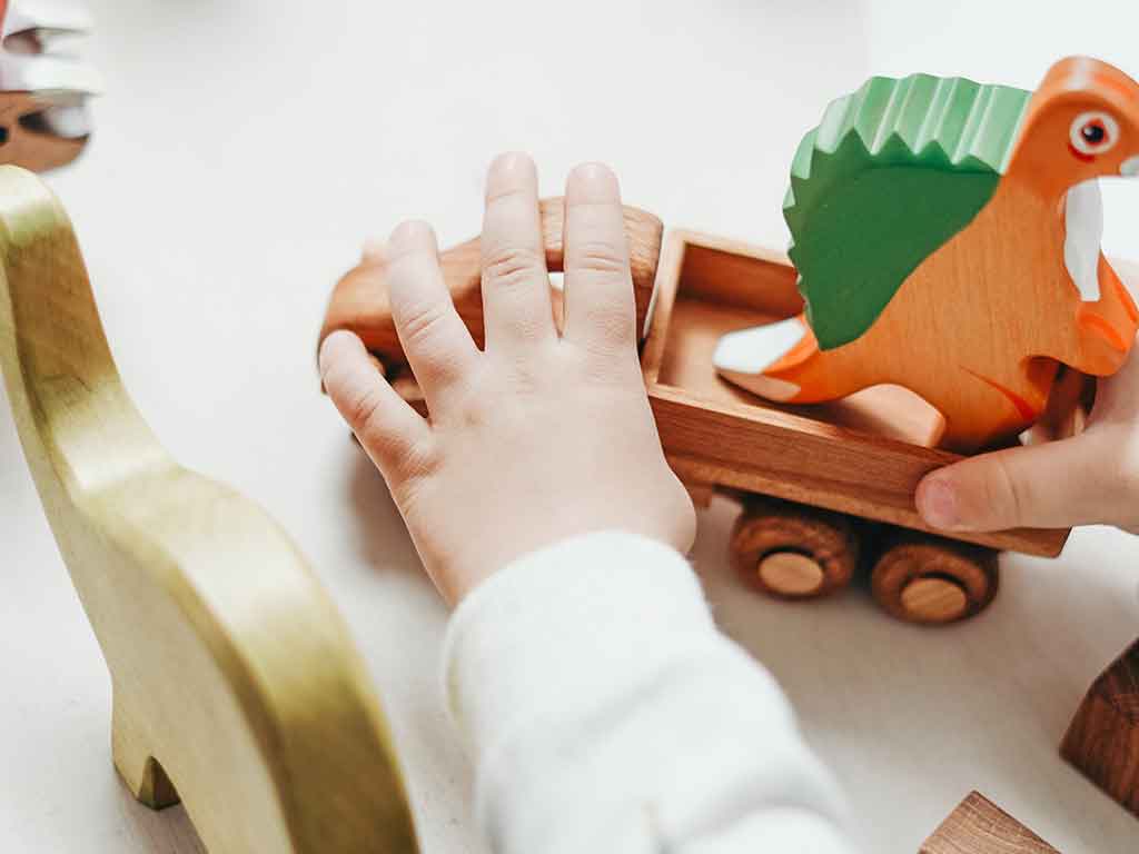 Das Foto zeigt die Hände von einem Kleinkindes, das mit Holzspielzeug spielt, als Vorschau für den Eltern-Workshop Freies Spiel.