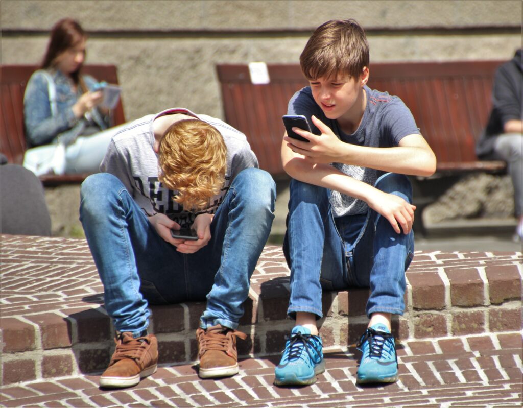 das Bild zeigt zwei Jungs, die sich über ihr Handy beugen